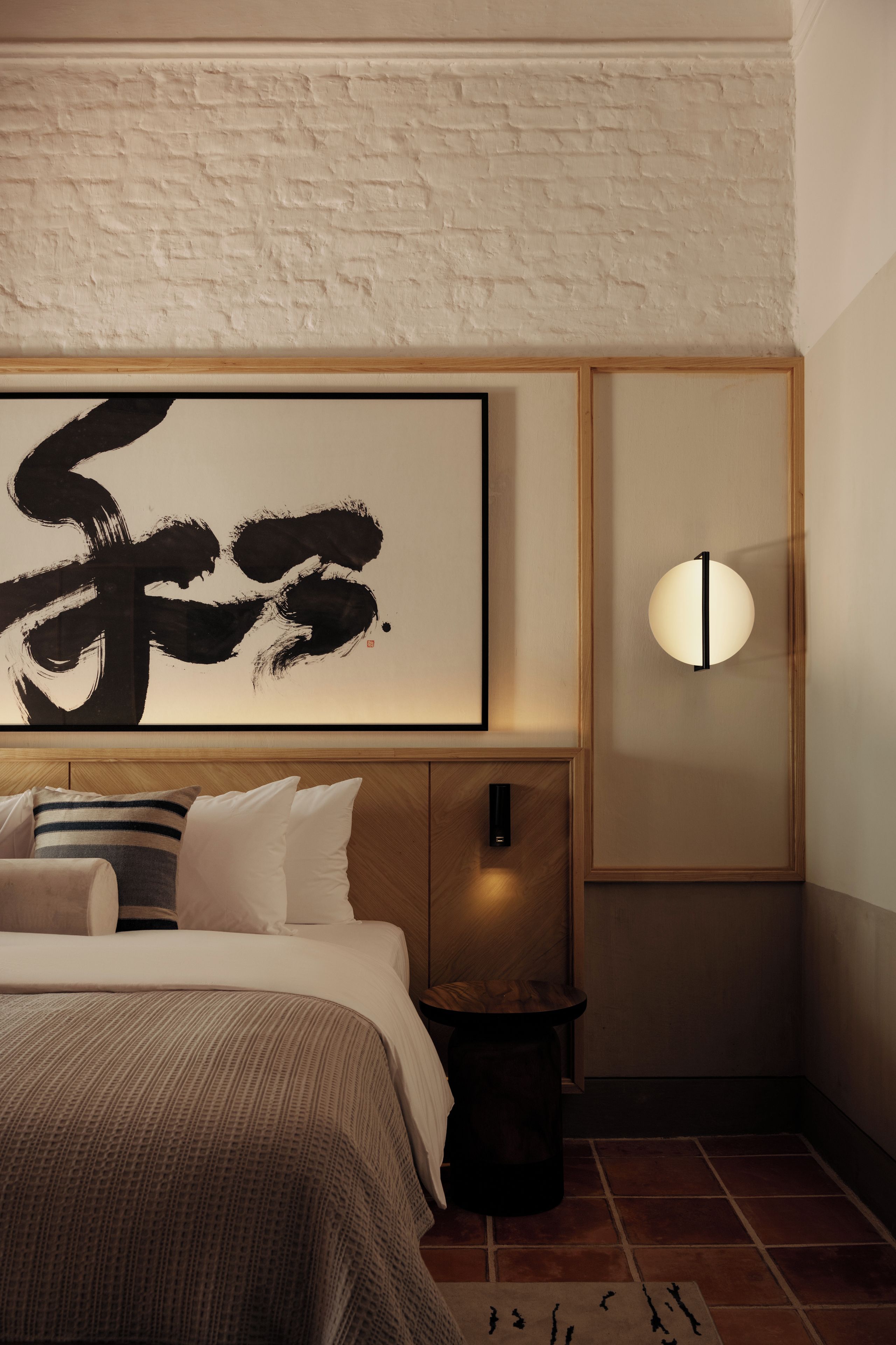 Un dormitorio con una cama grande, una mesita de noche, una lámpara de pared y una obra de arte enmarcada.