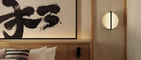 Un dormitorio con una cama grande, una mesita de noche, una lámpara de pared y una obra de arte enmarcada.