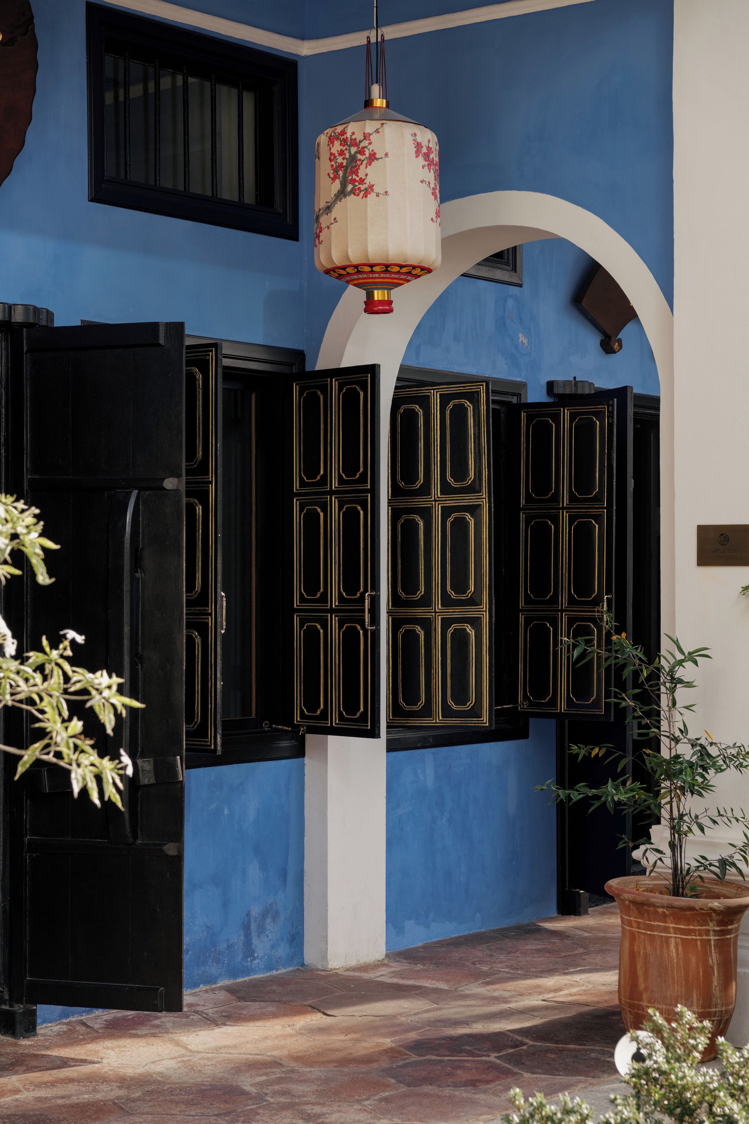 A traditional building with blue walls, black doors with gold trim, and a hanging lantern.