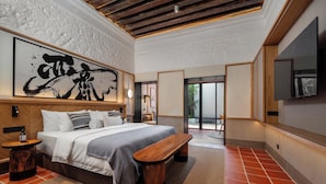 A modern bedroom with a large bed, a wooden bench, a large abstract painting, and a TV mounted on the wall. - Cheong Fatt Tze - The Qing Suites (George Town)