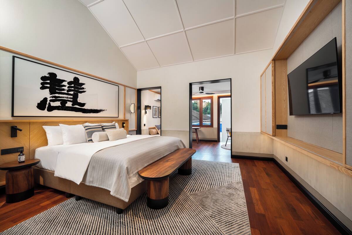 A modern hotel room with a large bed, wooden bench, and a TV mounted on the wall.