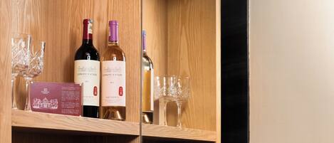 A kitchen with wooden shelves, wine bottles, glasses, a coffee maker, and a decorative bowl.