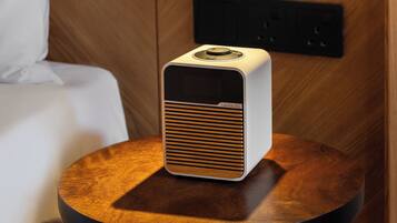 Una habitación moderna con un panel de pared de madera, una mesita de noche con un altavoz blanco y un aplique negro fijado a la pared.