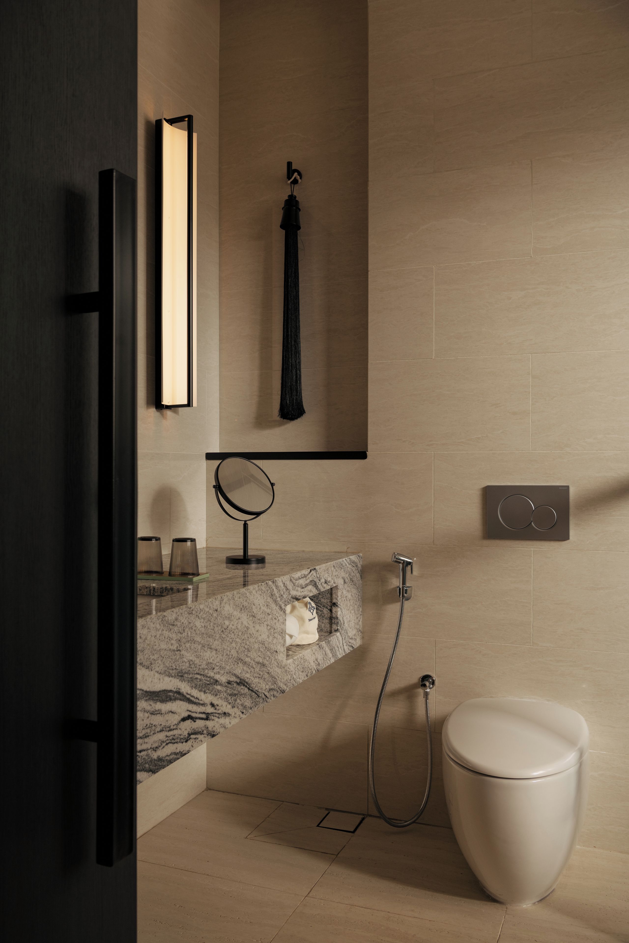Un baño moderno con encimera de mármol, un espejo redondo, toallero, inodoro y panel de control de ducha.