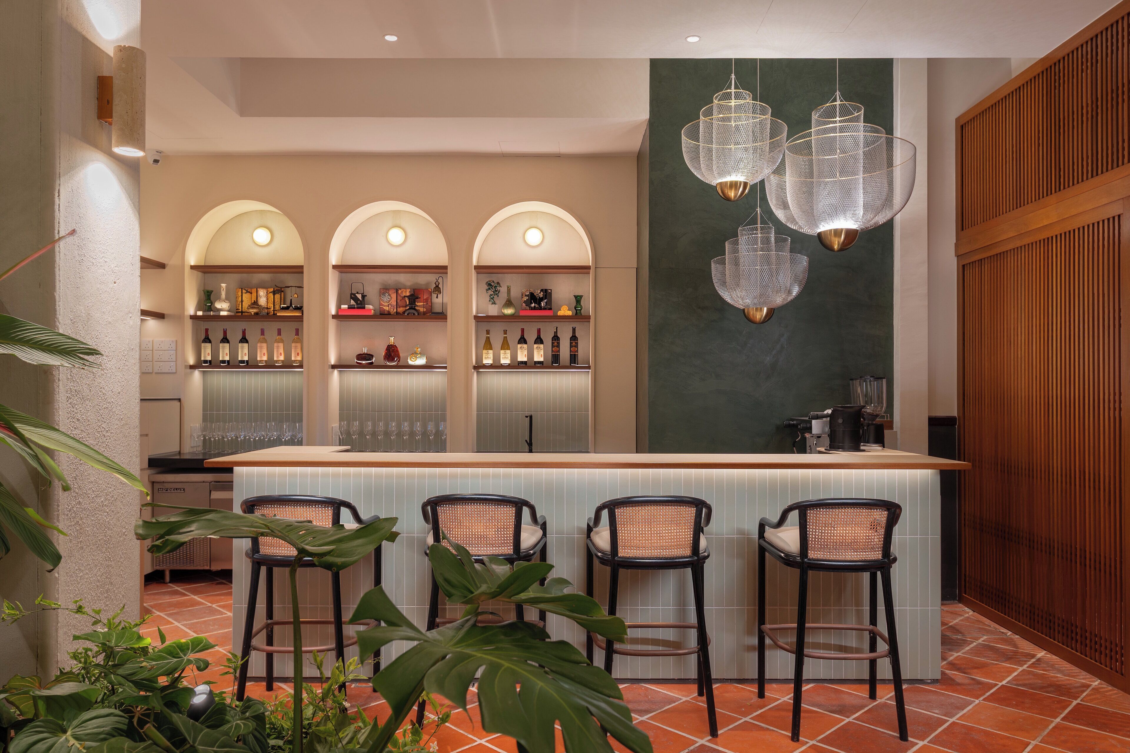 A bar area with a counter, three shelves of bottles, and four bar stools.