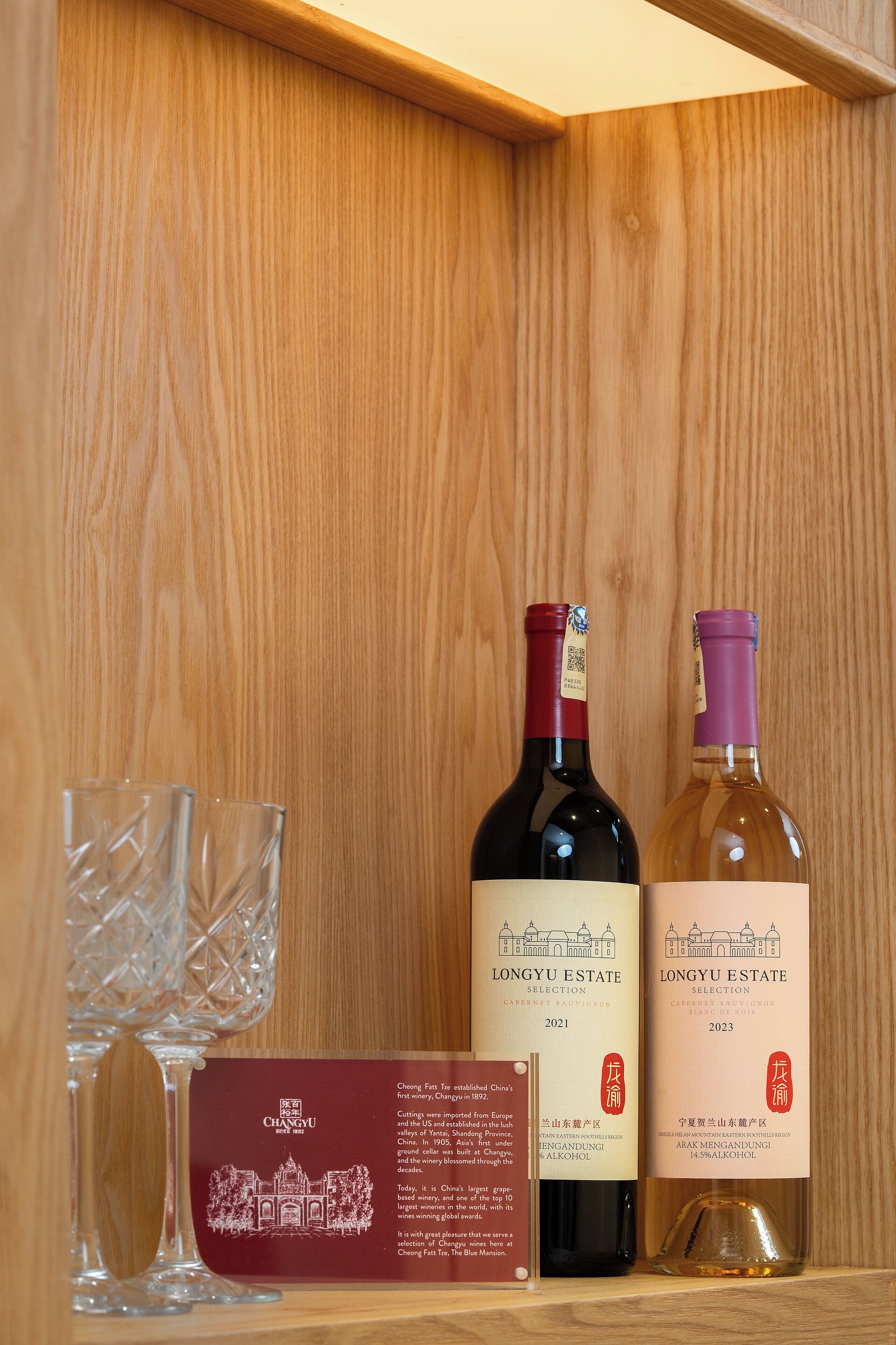Ein Holzregal mit zwei Flaschen Wein vom Weingut Longyu und einem Glas.