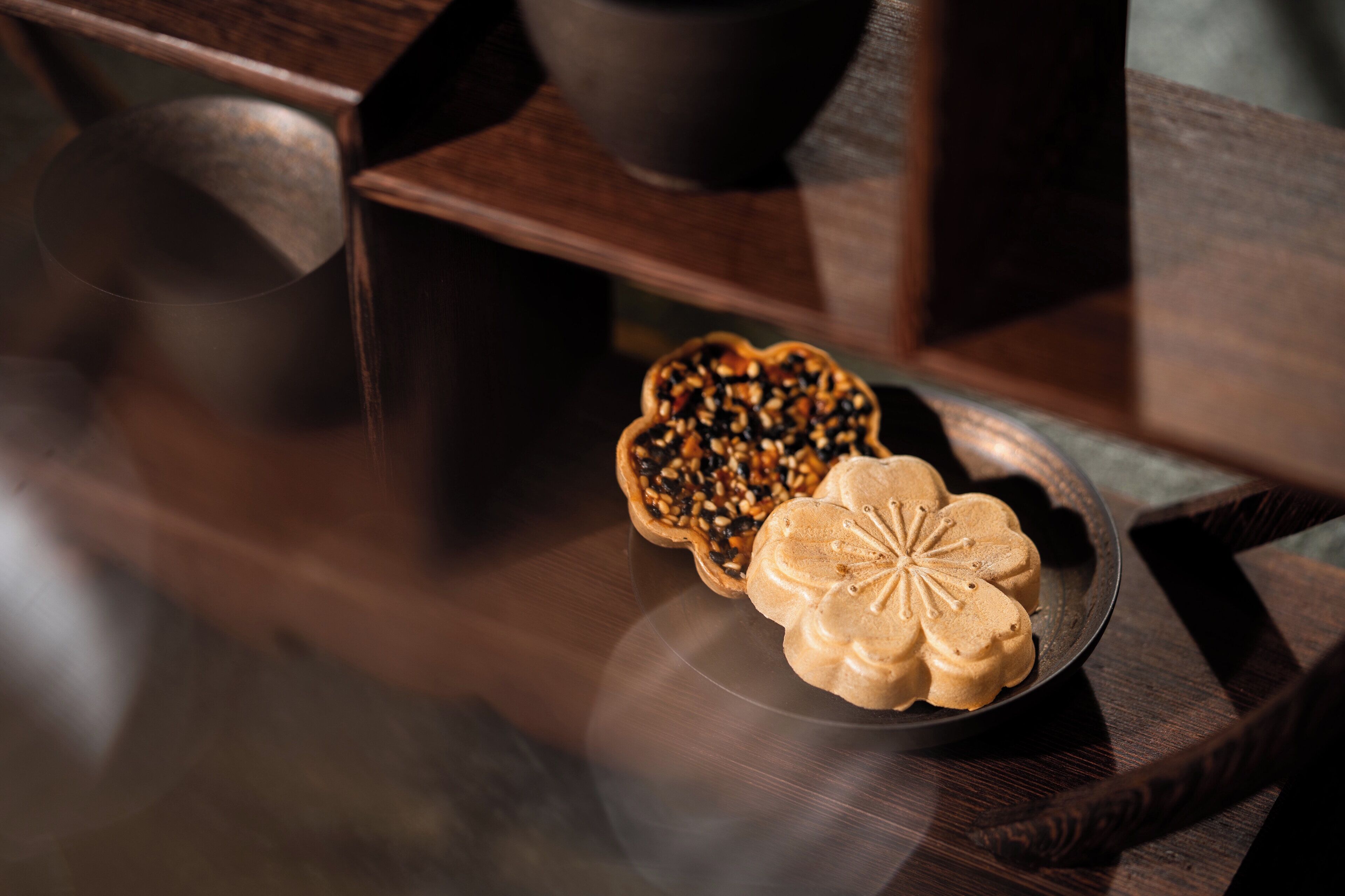 A wooden table with a plate of mooncakes and a decorative bowl.
