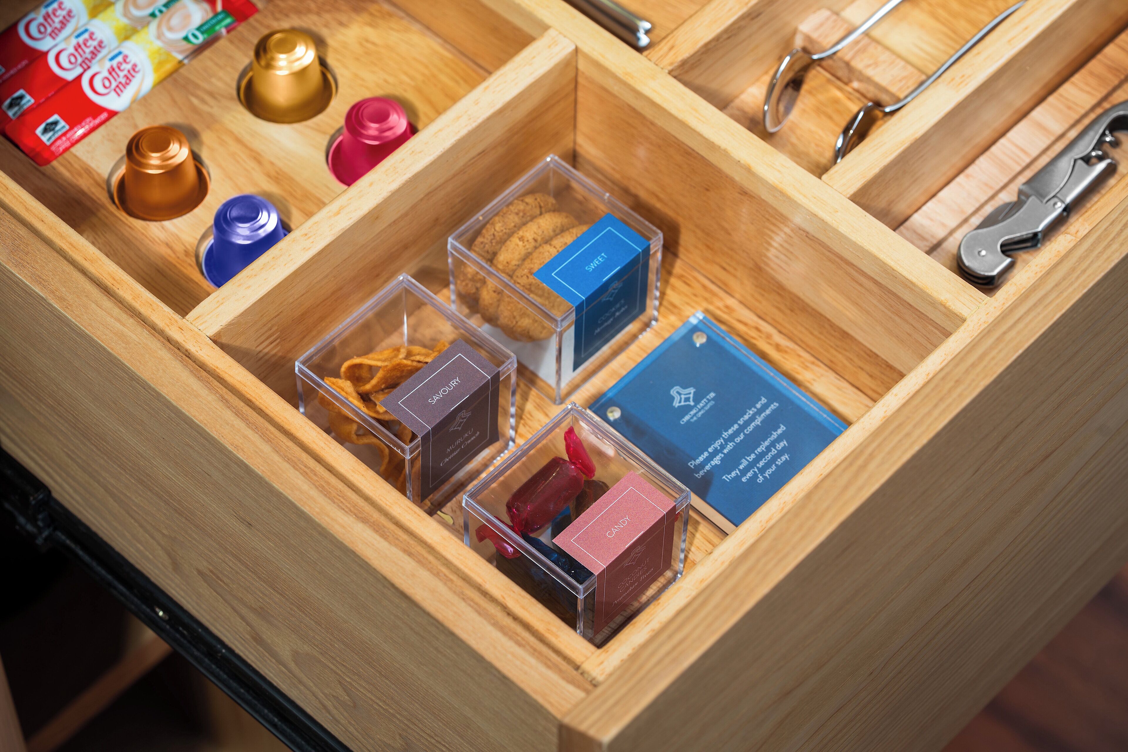 Eine Holzkassette mit Fächern, die verschiedene Gegenstände wie eine Kaffeedose, eine Schere und mehrere kleine Behälter mit unterschiedlichen Beschriftungen enthalten.