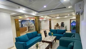 Een moderne woonkamer met blauwgroene banken, marmeren salontafels en een groot schilderij aan de muur.