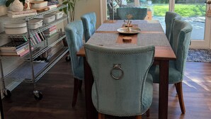 Een eetruimte met een houten tafel, teal bekleden stoelen en een metalen wandplank met keukengerei.