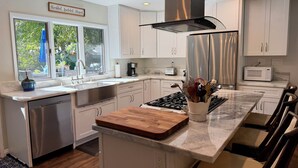 Een moderne keuken met witte kasten, roestvrijstalen apparatuur, een centraal eiland met een houten aanrechtblad en een raam met uitzicht op groen.