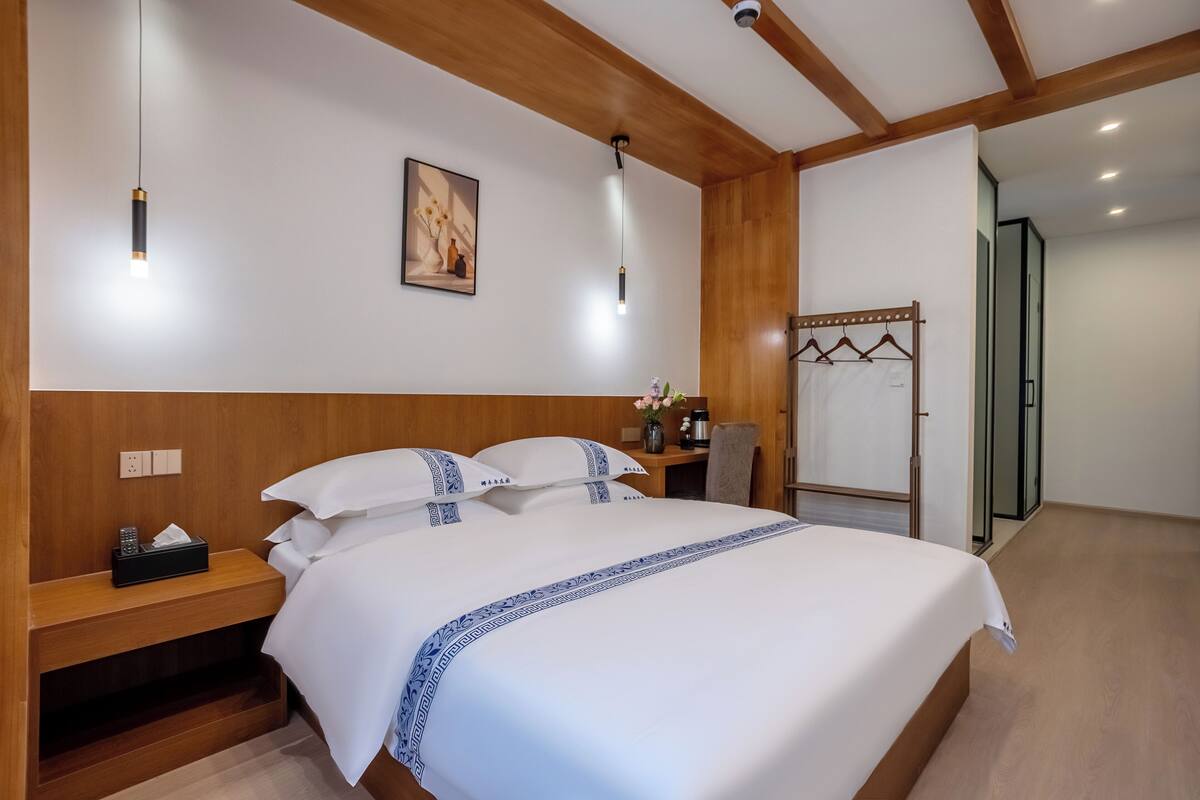 Una habitación de hotel con una cama grande, cabecero de madera, mesitas de noche y un perchero.