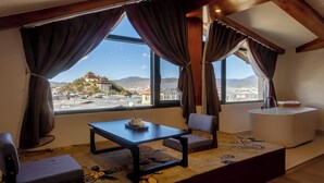 Una habitación con un ventanal grande, una mesa con tetera, una silla, un sofá y un lavamanos pequeño y blanco.