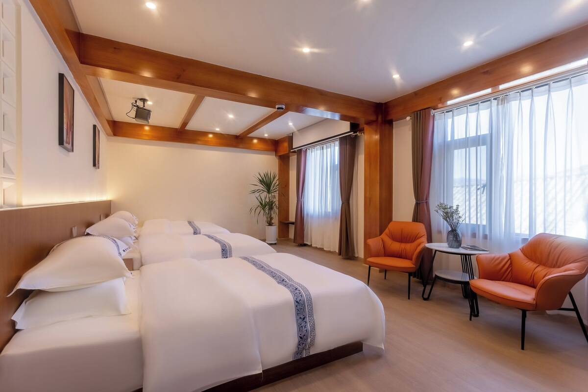 Habitación de hotel con una cama grande, dos sillas, una mesita pequeña y una planta en maceta.