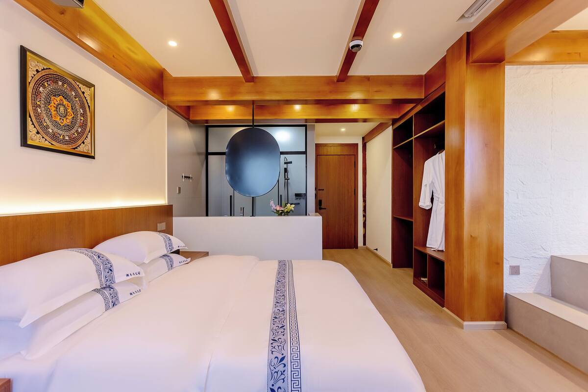 Un dormitorio moderno con una cama grande, vigas de madera en el techo, un vestidor y un baño con un espejo amplio.