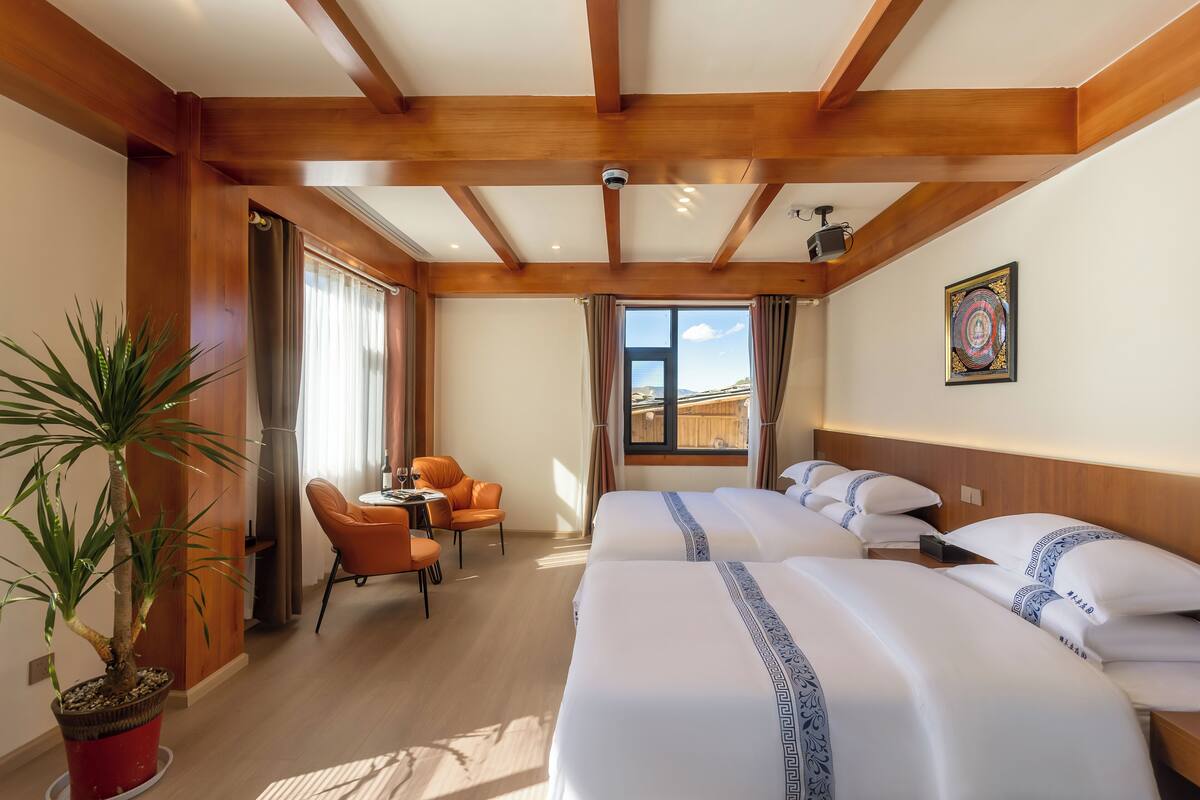 Habitación de hotel con vigas de madera, dos camas con ropa de cama blanca, una planta en maceta, un escritorio con silla y una ventana con cortinas.