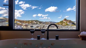 Un baño con un ventanal grande, una bañera y vistas a un paisaje urbano con arquitectura tradicional.