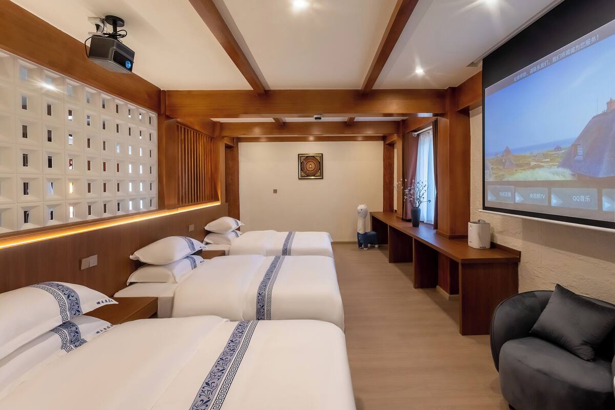 Habitación de hotel con tres camas, una pantalla grande y techo de madera.