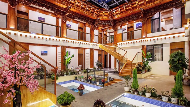 Un amplio atrium con varios niveles, escaleras de madera y una zona de piscina central rodeada de macetas con plantas y flores.