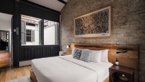 Ein Schlafzimmer mit einem großen Bett, einem Holzkopfteil, einem Nachttisch, einem Bilderrahmen mit einem abstrakten Gemälde und Blick durch eine offene Tür.