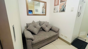 Quarto com sofá cinza, um espelho grande e decoração na parede.