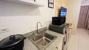 Uma cozinha compacta com pia de aço inoxidável, micro-ondas e fogão. Há um letreiro com a palavra 'HOME' sobre a pia e uma frase emoldurada na parede.