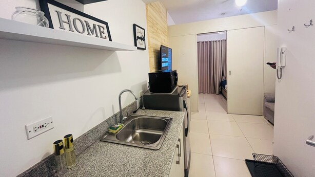 Cozinha moderna com micro-ondas embutido, pia e máquina de café. Há um armário pequeno e uma prateleira com a placa 'HOME'.