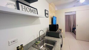 Uma cozinha moderna com bancada de granito, pia de aço inoxidável e micro-ondas preto. Uma placa com a palavra 'HOME' é visível na parede, e um laptop está sobre o micro-ondas.