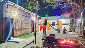 Un espace extérieur rustique avec un bâtiment à toit de chaume, un barbecue avec des flammes et un hamac.