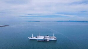 Un grand navire de croisière était amarré à un quai, sur des eaux calmes, avec une terre lointaine en arrière-plan.