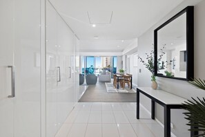 A modern, well-lit hallway with a glass door leading to a living area with a view of the cityscape. - Hilton Residences - Pool Views (Surfers Paradise)