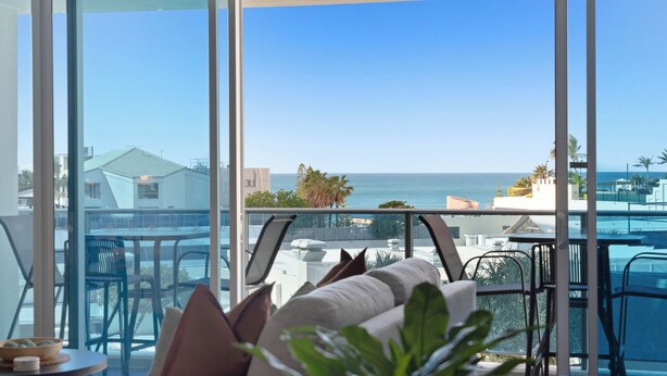 Et moderne hotelværelse med stor balkon, der giver udsigt over hav og bybillede.