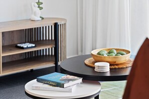 A round table with a bowl of green fruits, a book titled 'Italian Coast', and a decorative item on a shelf. - Hilton Residences - Pool Views (Surfers Paradise)