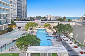 A rooftop pool area with lounge chairs, a swimming pool, and a view of the ocean. - Hilton Residences - Pool Views (Surfers Paradise)