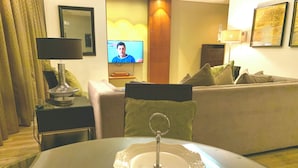 Uma sala de estar com televisão, sofá, mesa de jantar com jogo americano verde e luminária.