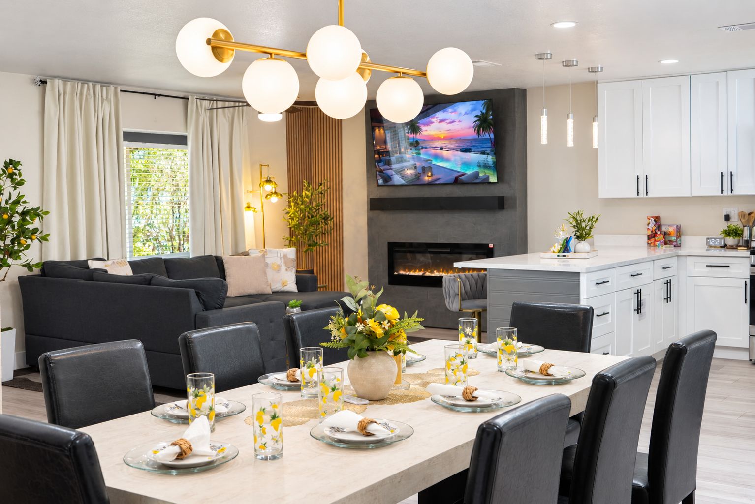 A modern living room with a fireplace, a dining area set for four, and a kitchen with white cabinets.