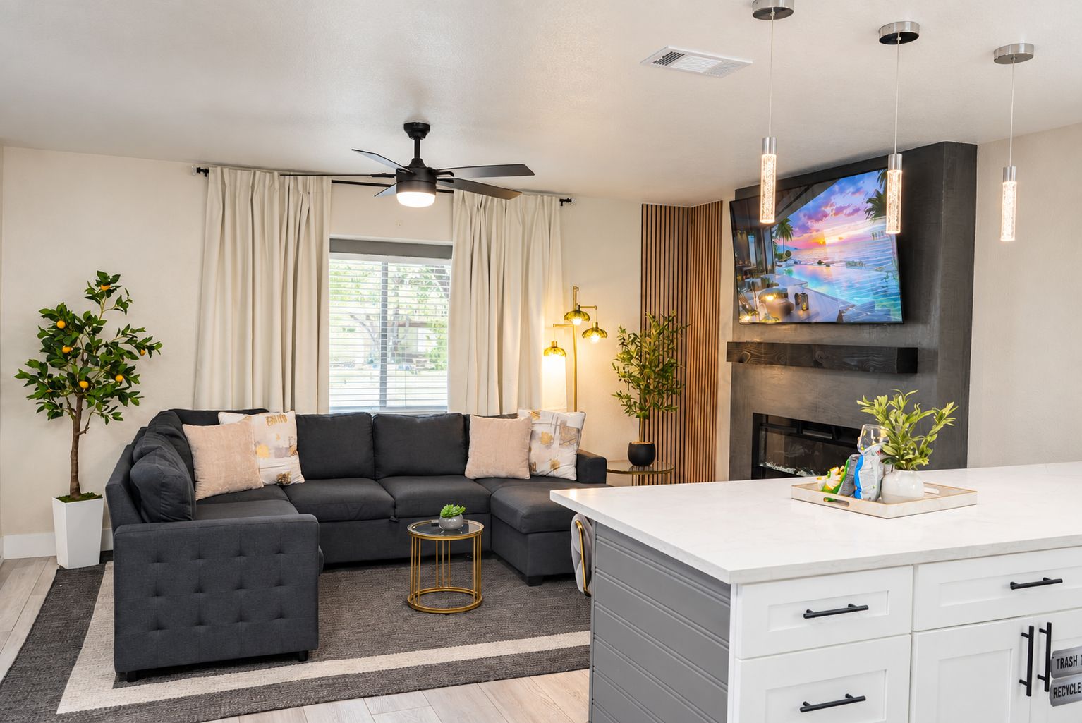 Una sala de estar moderna con un sofá seccional, un televisor de pantalla plana, una chimenea y una zona de comedor con encimera blanca.