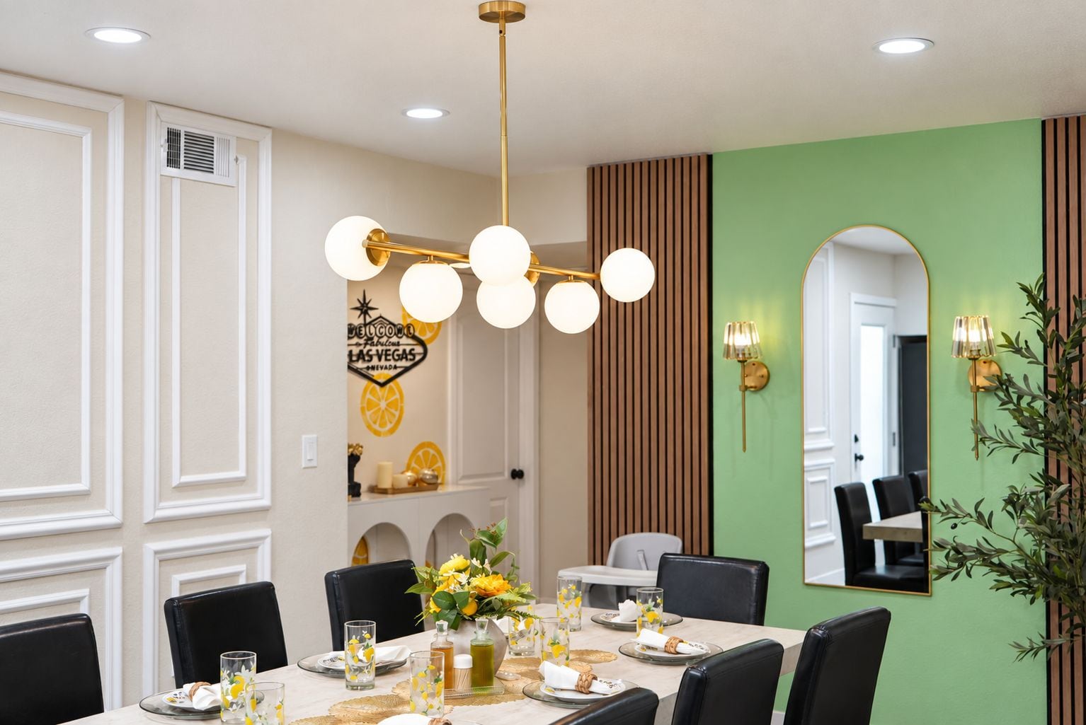 Un coin repas avec une table dressée pour quatre personnes, un lustre moderne et un miroir fixé au mur.