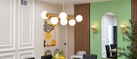 Un coin repas avec une table dressée pour quatre personnes, un lustre moderne et un miroir fixé au mur.