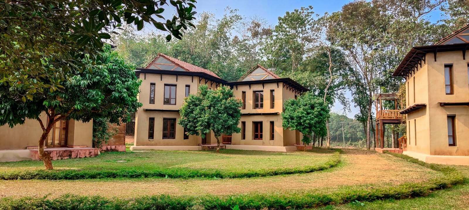 A two-story building with a flat roof and a balcony, surrounded by a well-maintained lawn and trees.