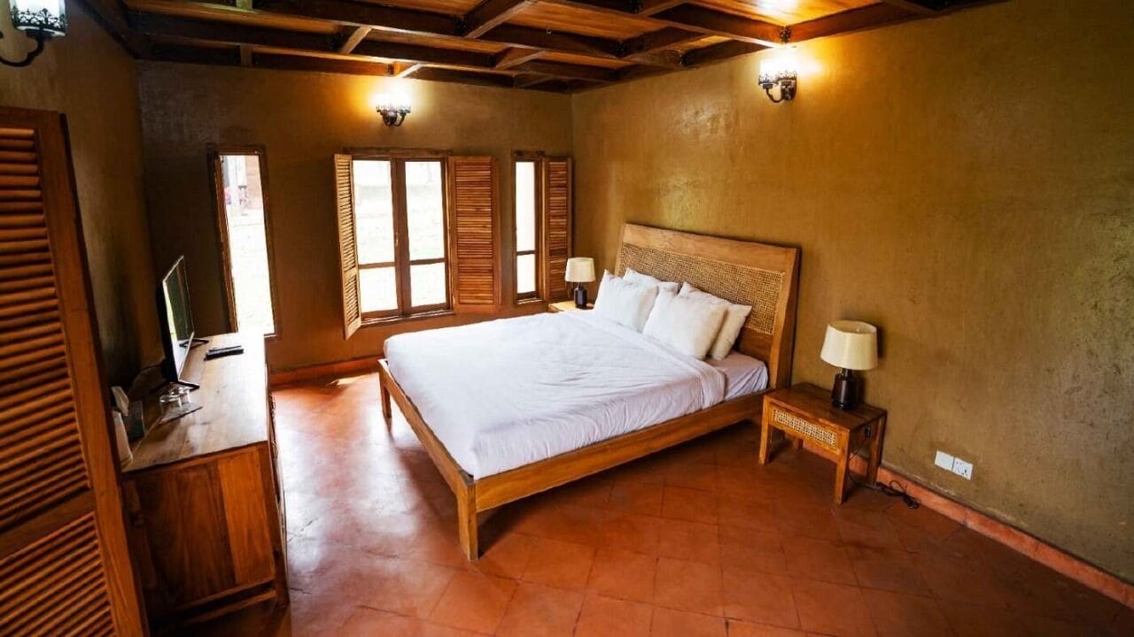 Un dormitorio con cama de madera, dos lámparas de noche, una mesita de noche y una ventana con contraventanas.