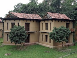Um edifício de dois andares com telhado de telhas e várias janelas. Duas árvores na frente do edifício.
