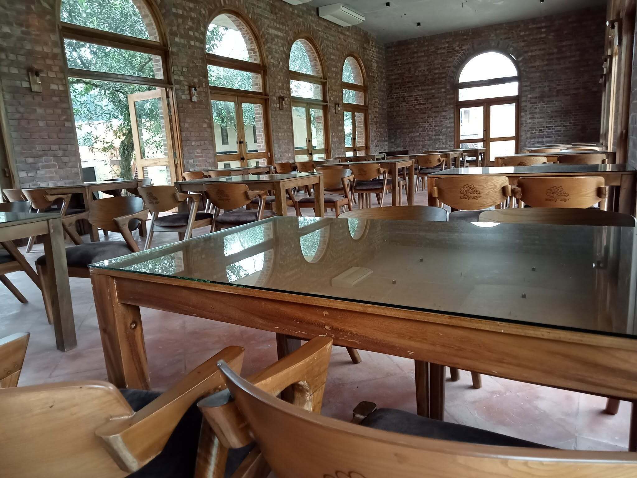 A spacious room with a large glass table surrounded by wooden chairs, brick walls, and large windows.