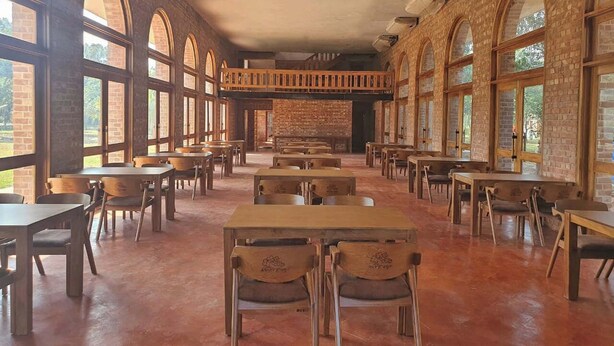 Un comedor amplio con paredes de ladrillo, ventanas arqueadas grandes y mesas y sillas de madera.