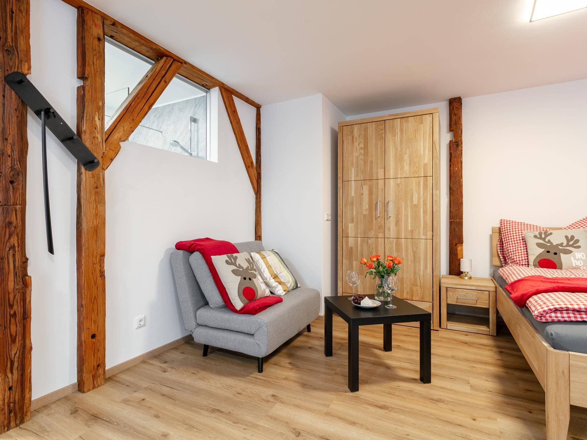 Une pièce chaleureuse avec une armoire en bois, un canapé gris et un lit agrémenté de coussins aux motifs festifs.