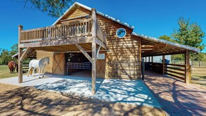 A wooden barn with a balcony, a covered entrance, and a fenced area with horses. - Historic Barn in Mississippi: Equestrian Getaway! (Tylertown)