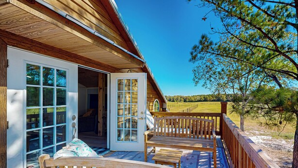 A wooden cabin with a deck, a large glass door, and a view of the outdoors. - Historic Barn in Mississippi: Equestrian Getaway! (Tylertown)