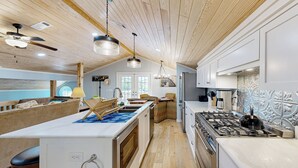 A modern kitchen with wooden ceiling beams, a central island with a sink, and a gas stove. - Historic Barn in Mississippi: Equestrian Getaway! (Tylertown)