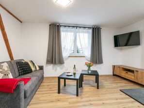 A modern living room with a grey sofa, a small table with a vase of flowers, a wine glass, and a flat-screen TV mounted on the wall. - Stylish holiday apartment in Brixen im Thale (Brixen im Thale)