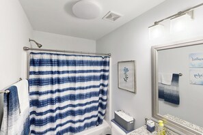 A bathroom with a striped shower curtain, a sink with a marble countertop, and a mirror with a towel hanging on the wall.